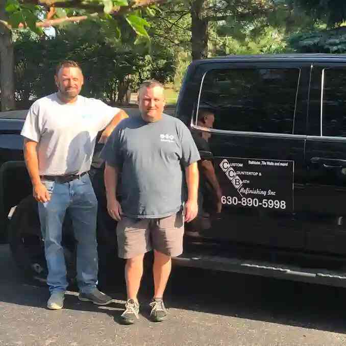 The image shows two men posing for a picture outside on a sunny day standing in front of a black pickup truck labeled Custom Countertop & Bath for CCB Refinishing.