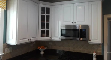 Learn more about our refinishing process. The image shows a kitchen with refinished cabinets and a microwave.
