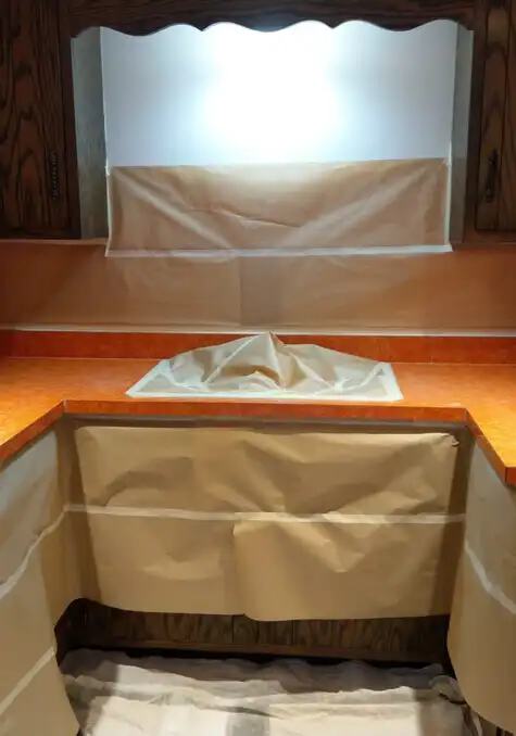The image shows a kitchen sink that has been covered with paper to protect the surfaces prior to refinishing the orange-colored countertop.